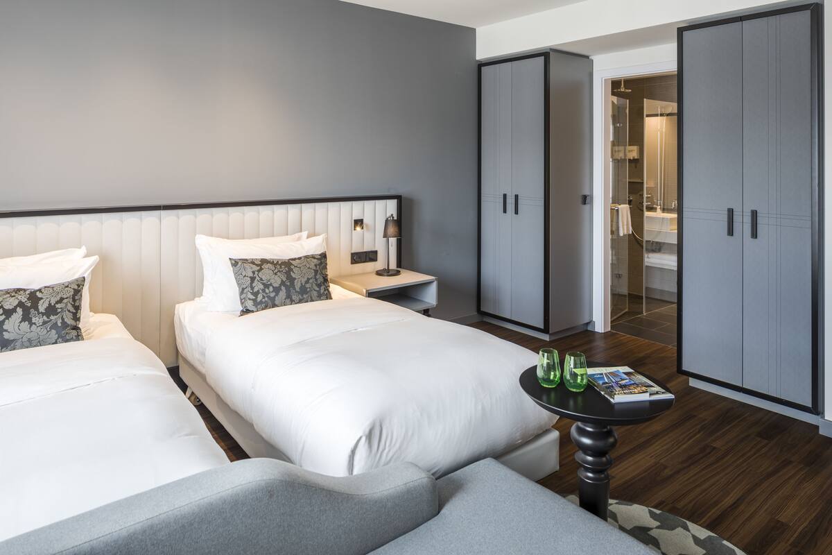 Une chambre d’hôtel avec deux lits, une petite table avec des verres verts et une armoire.