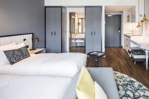 Una camera d'albergo moderna con un letto grande, un'area salotto con divano, un tavolino e vista sul bagno e sulla cucina.