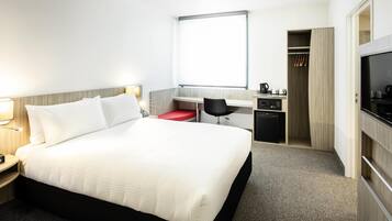 Une chambre d’hôtel équipée d’un lit, d’un bureau, d’une chaise, d’une kitchenette et d’un téléviseur.