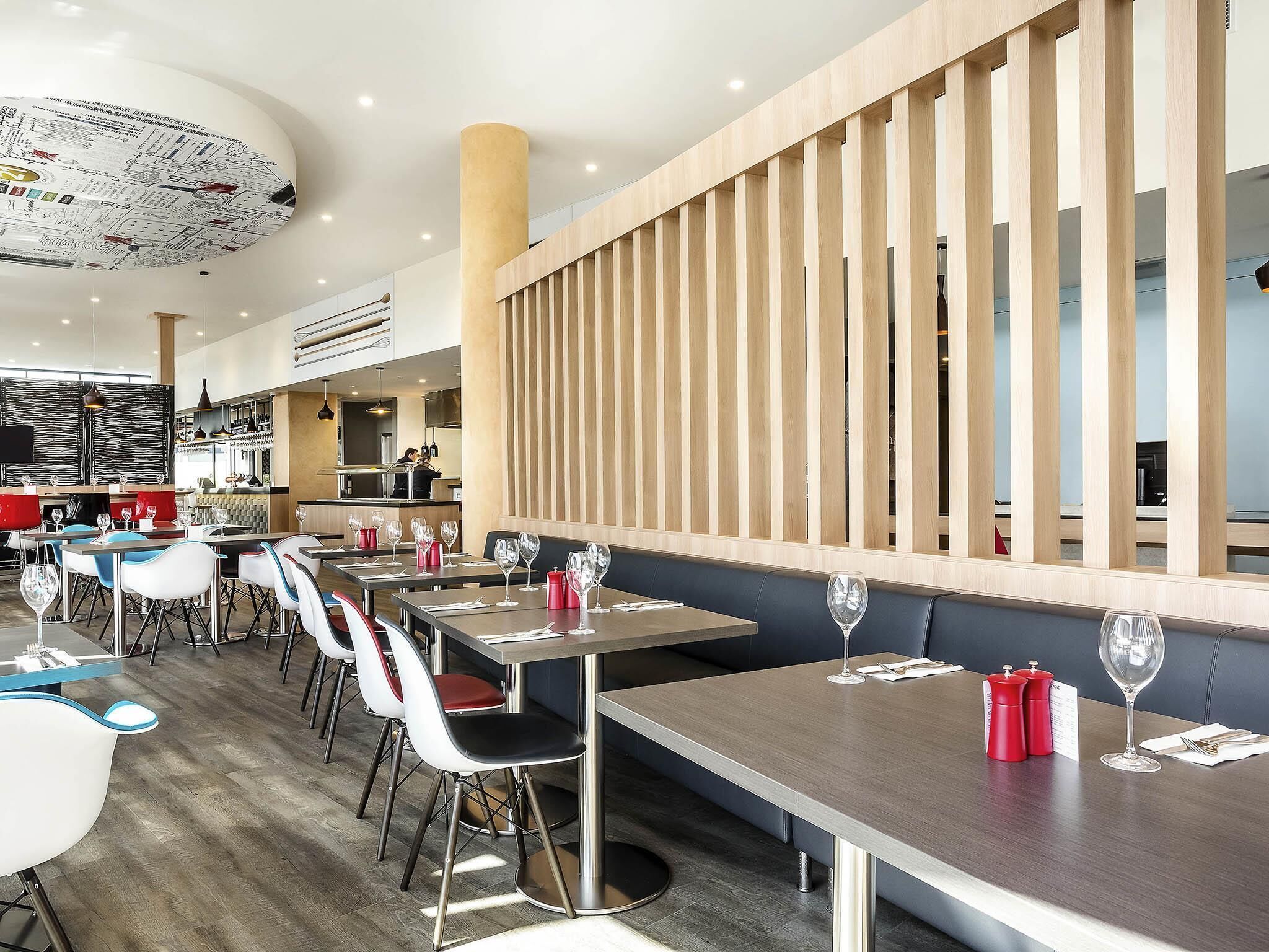 Et moderne restaurantinteriør med høje borde, stole og et barområde.