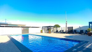 A swimming pool with lounge chairs and a pergola, surrounded by a white fence and a clear sky. - ibis Mackay (South Mackay)