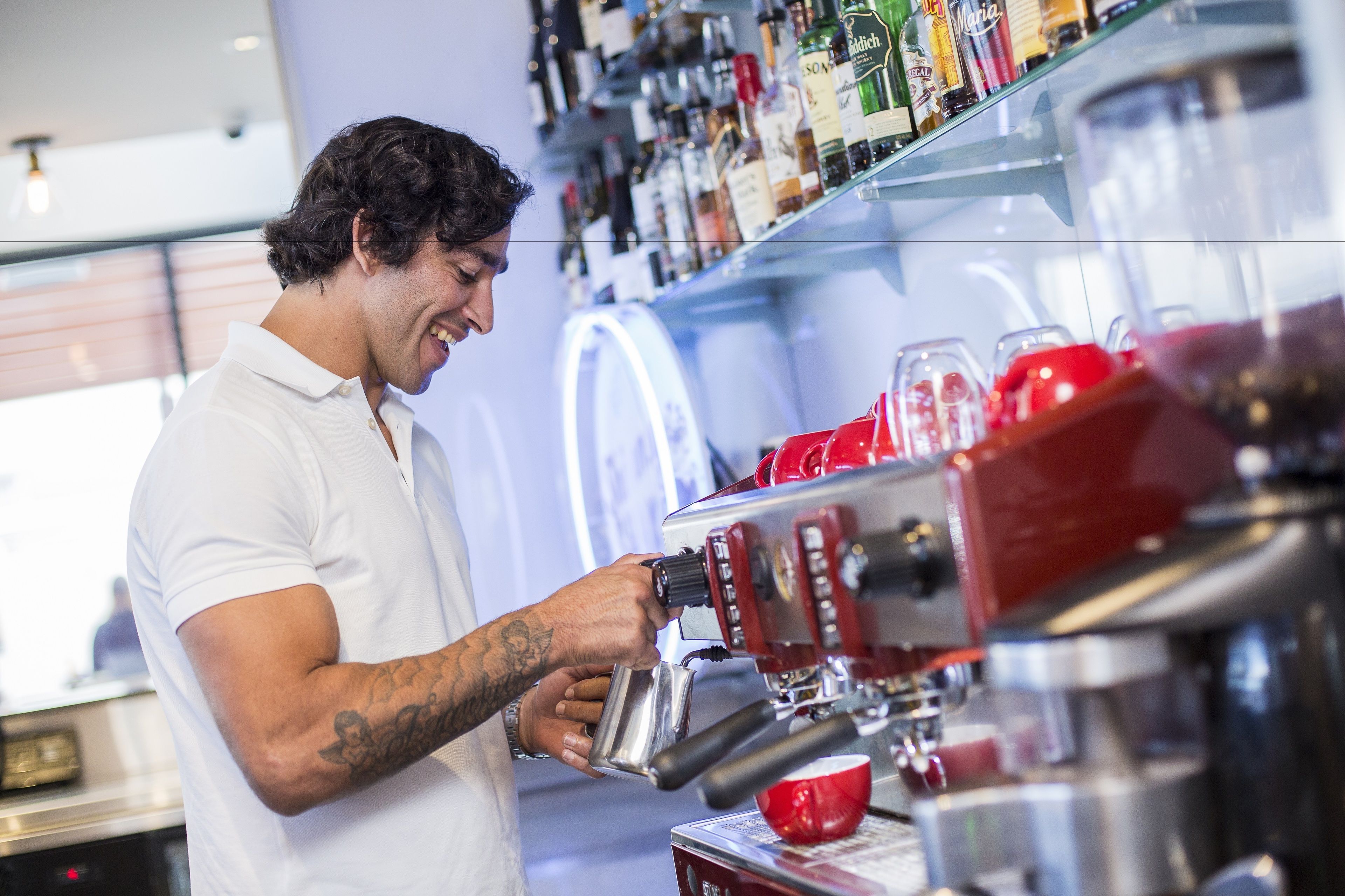Een barista maakt koffie met een espressoapparaat, een koffiekop en diverse flessen op de achtergrond.