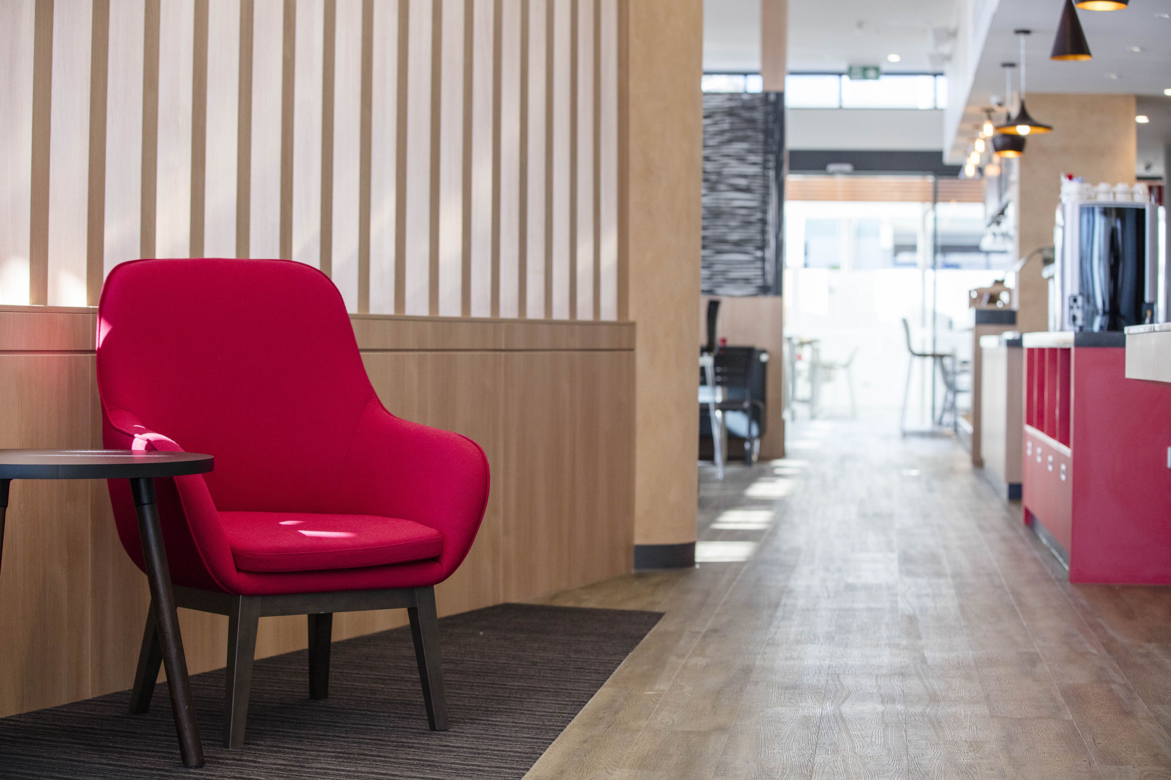 A modern interior with a red chair and a small table, wooden paneling, and a visible counter area.