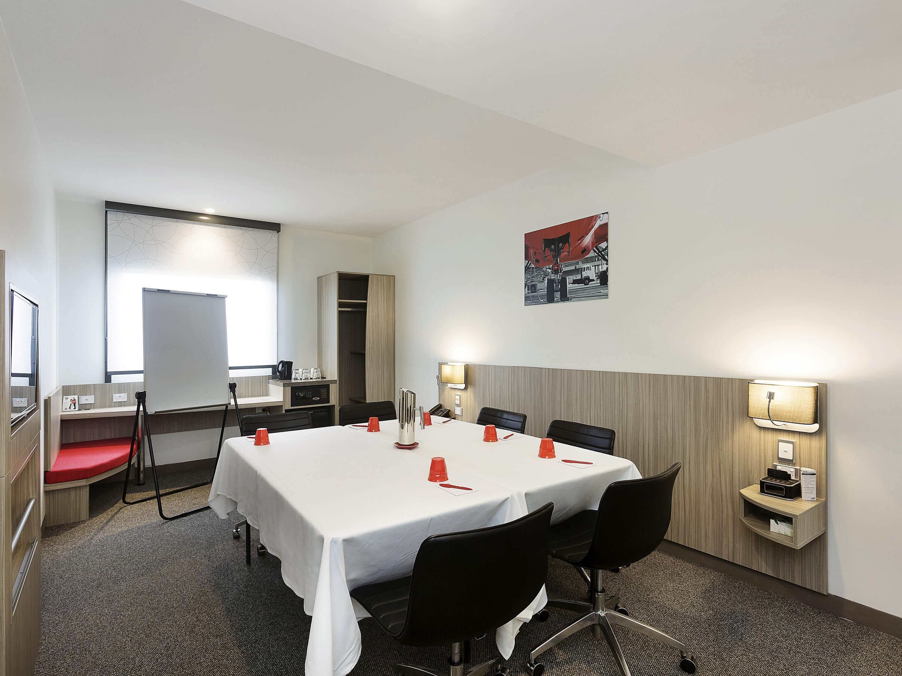 Ein Konferenzraum mit weißem Tisch, schwarzen Stühlen und roten Tassen.