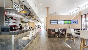 A modern bar area with a bar counter, stools, and a television screen displaying sports. - ibis Mackay (South Mackay)