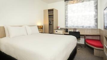 Quarto de hotel com uma cama grande, uma mesa, uma cadeira e um guarda-roupa.