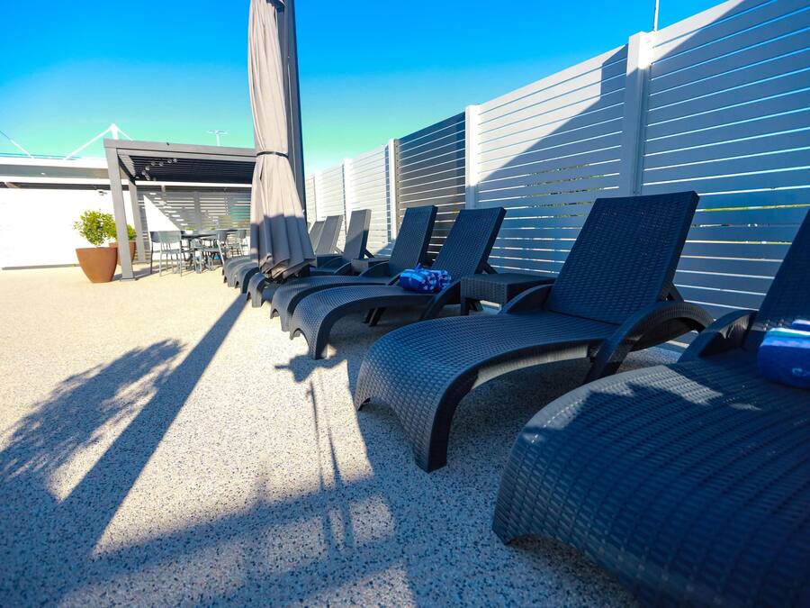 A row of outdoor lounge chairs with a pergola overhead, a potted plant, and a clear blue sky.