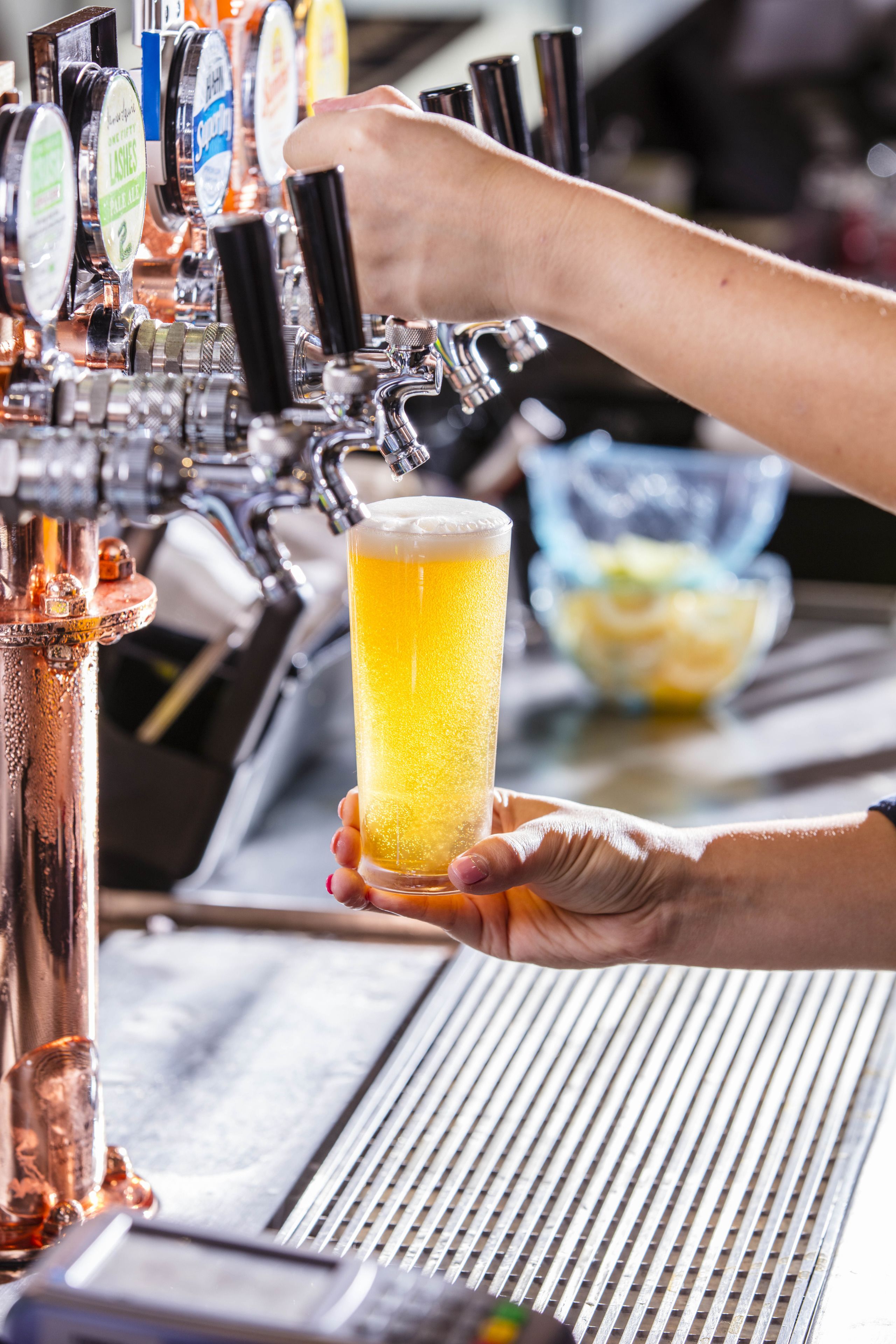 A hand holding a glass of beer in front of a tap with multiple beer options.