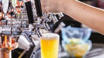 A hand holding a glass of beer in front of a tap with multiple beer options.