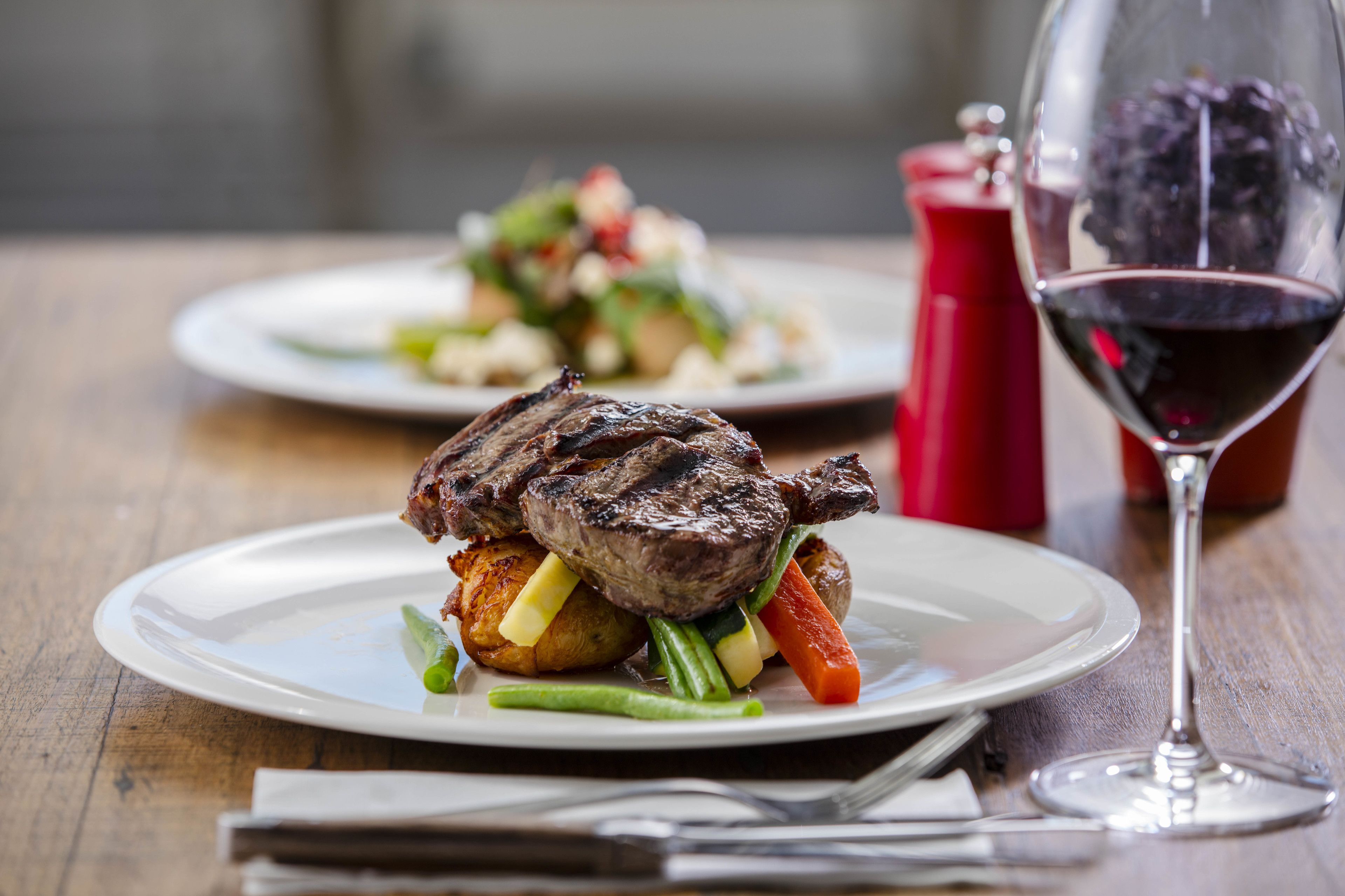 Une assiette de steak accompagné de légumes et un verre de vin rouge sur une table en bois.