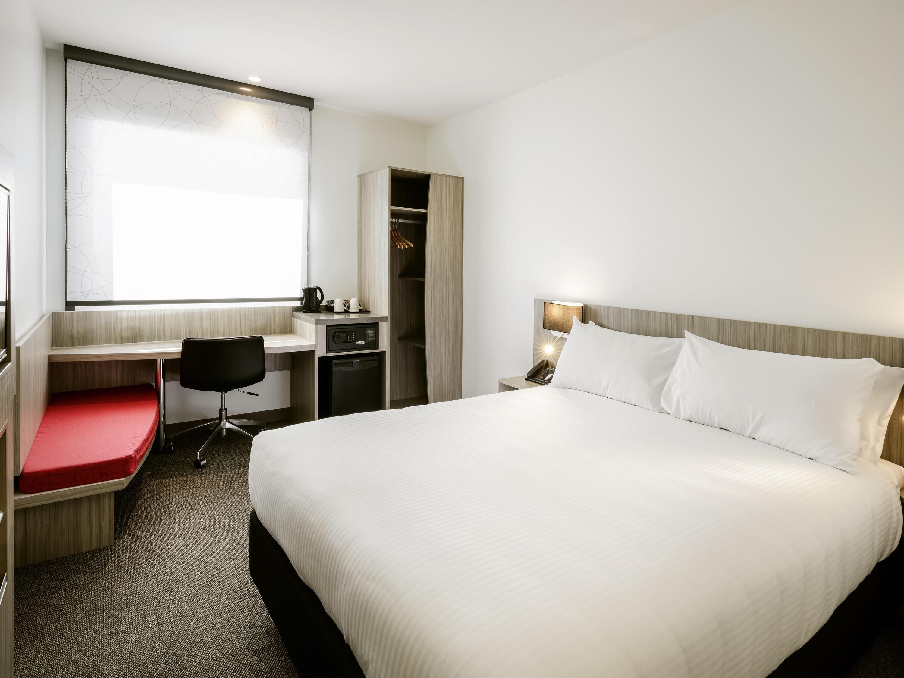 A hotel room with a bed, desk, chair, and a wardrobe.