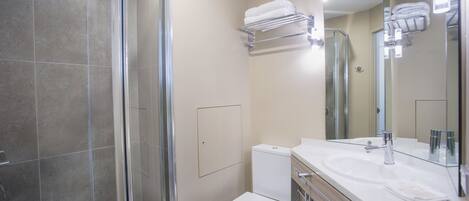 Un baño moderno con cabina de ducha de vidrio, inodoro blanco y tocador con espejo.