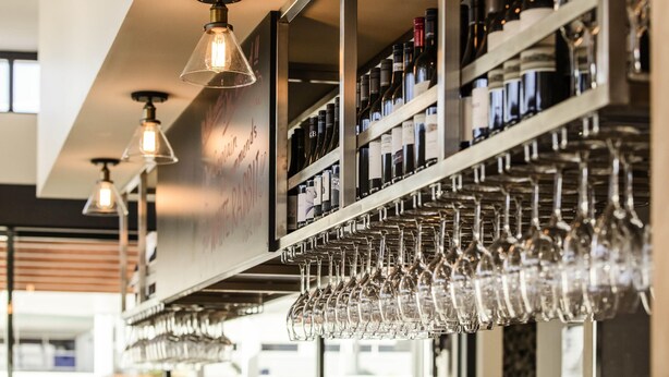 A bar area with shelves of wine bottles and a rack of wine glasses. - ibis Mackay (South Mackay)