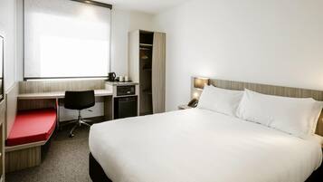 A hotel room with a bed, a desk with a chair, a wardrobe, and a television.
