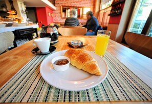 A dining table with a croissant, a cup of coffee, and a glass of orange juice. - Dream Hotel (Tirana)
