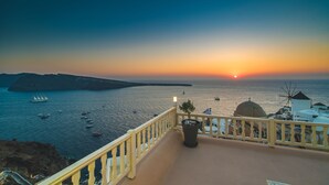 Vista costera con atardecer, barcos y un balcón con planta en maceta.