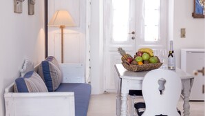 Una habitación acogedora con un sofá blanco, una mesa con fruta y vasos, y una lámpara.