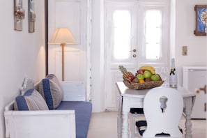 Una habitación acogedora con un sofá blanco, una mesa con fruta y vasos, y una lámpara.