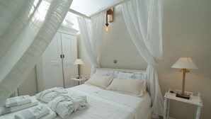 Un dormitorio con una cama, cortinas blancas, una mesita de noche con lámpara y una puerta.