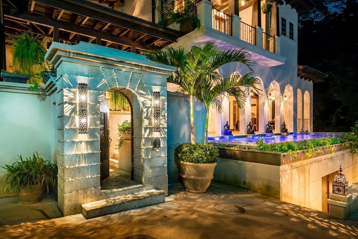 Un espacio exterior bien iluminado con un arco de piedra, una fuente y una piscina.