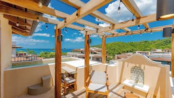 A wooden deck with a pool, outdoor seating, and a view of the ocean and greenery.