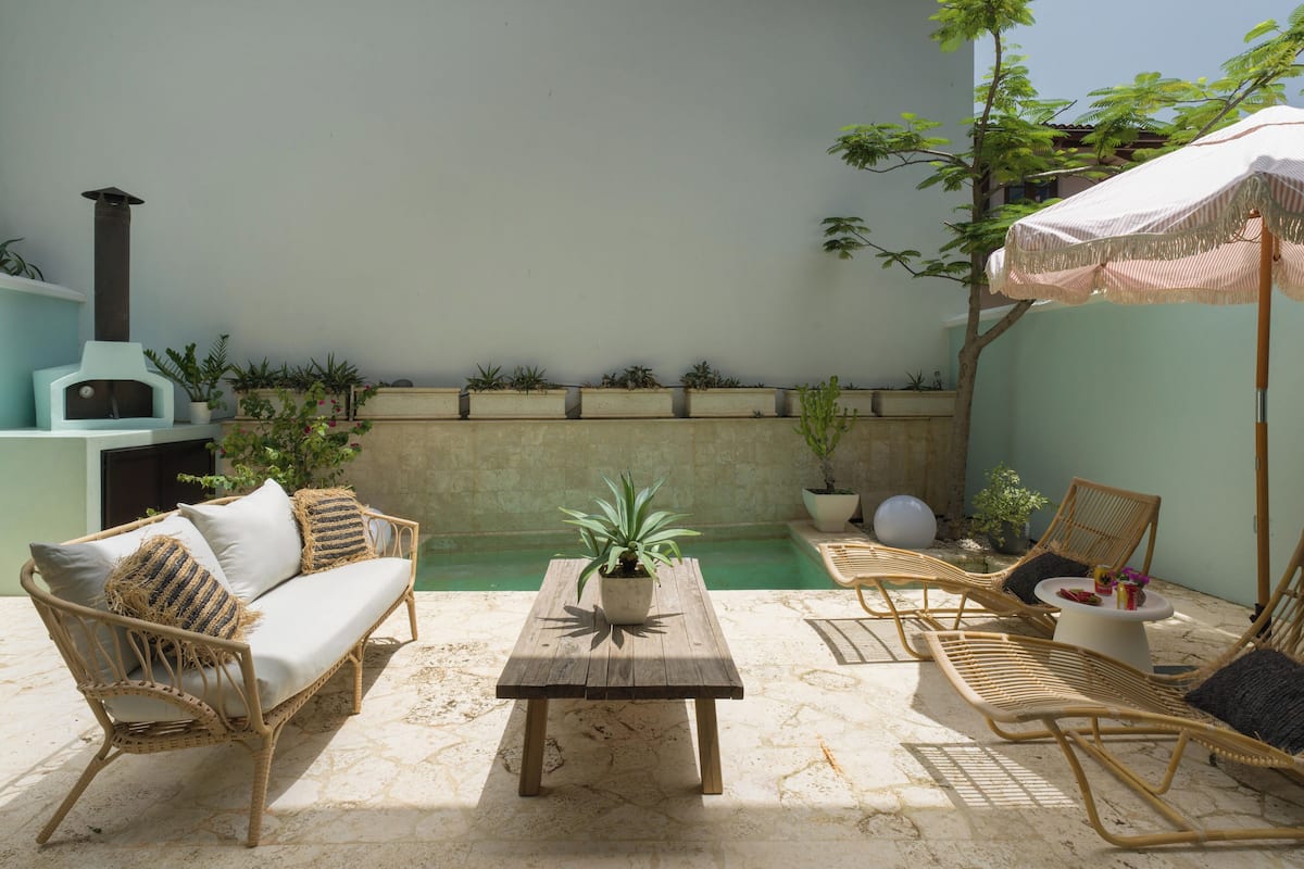 Un patio con un sofá, sillas, una mesa, una planta en maceta y una pequeña fuente.