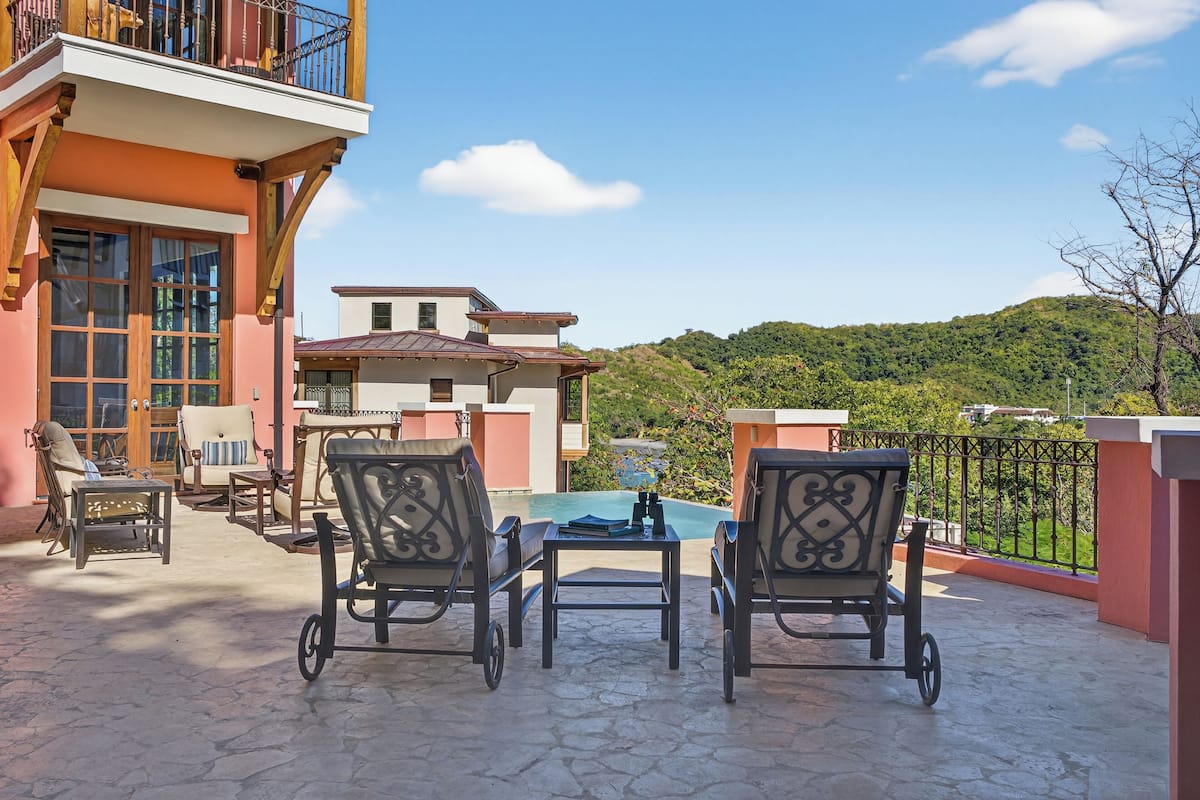 Un patio con mobiliario exterior, piscina y vistas a una colina.
