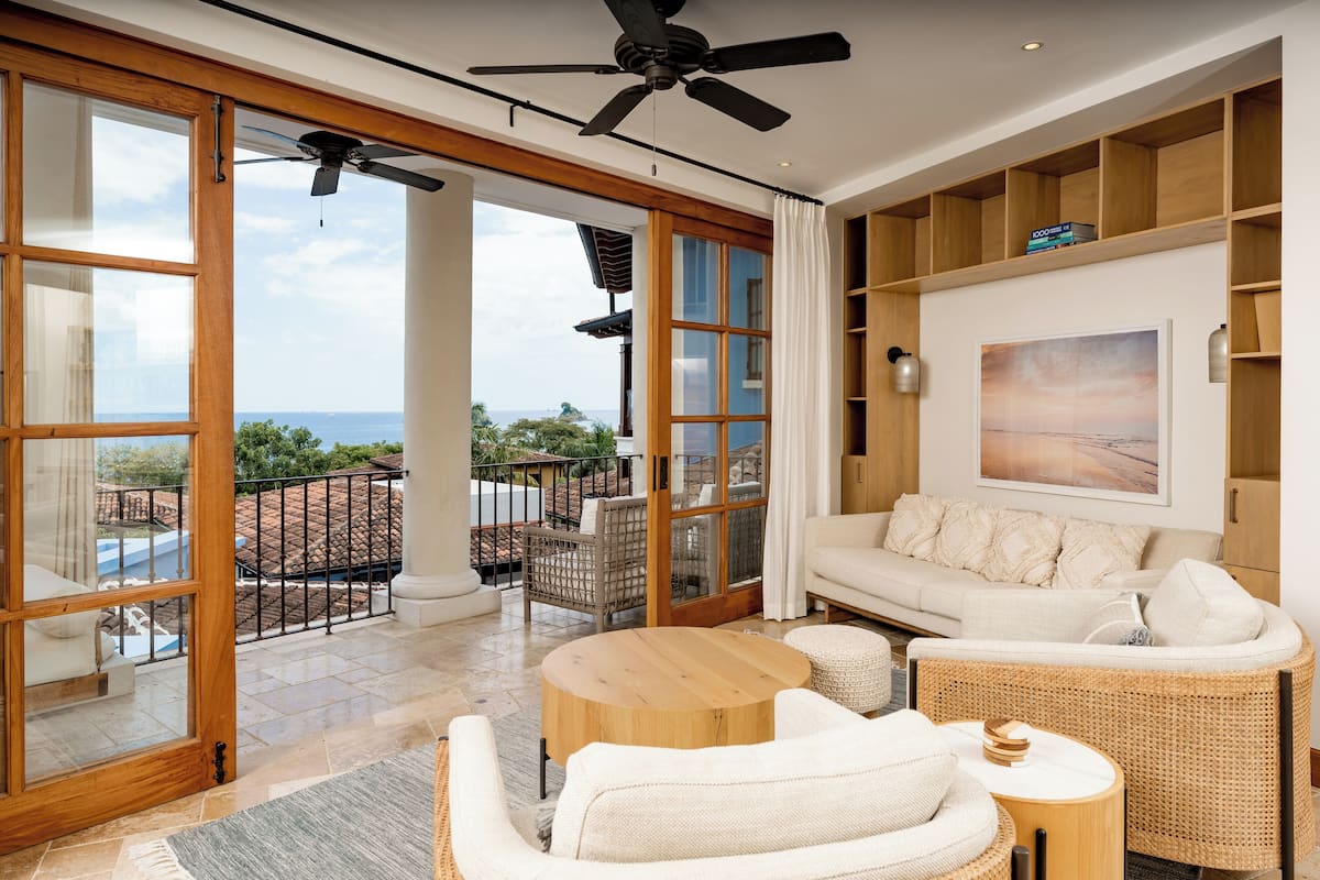 Amplia sala de estar con un ventanal grande, ventilador de techo, sofá y mesa de comedor.