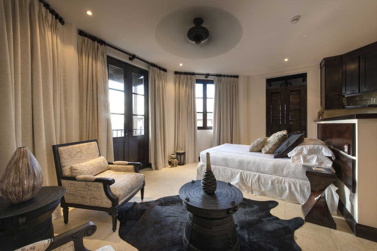 Un dormitorio con cama, una silla, una mesa y un florero decorativo.