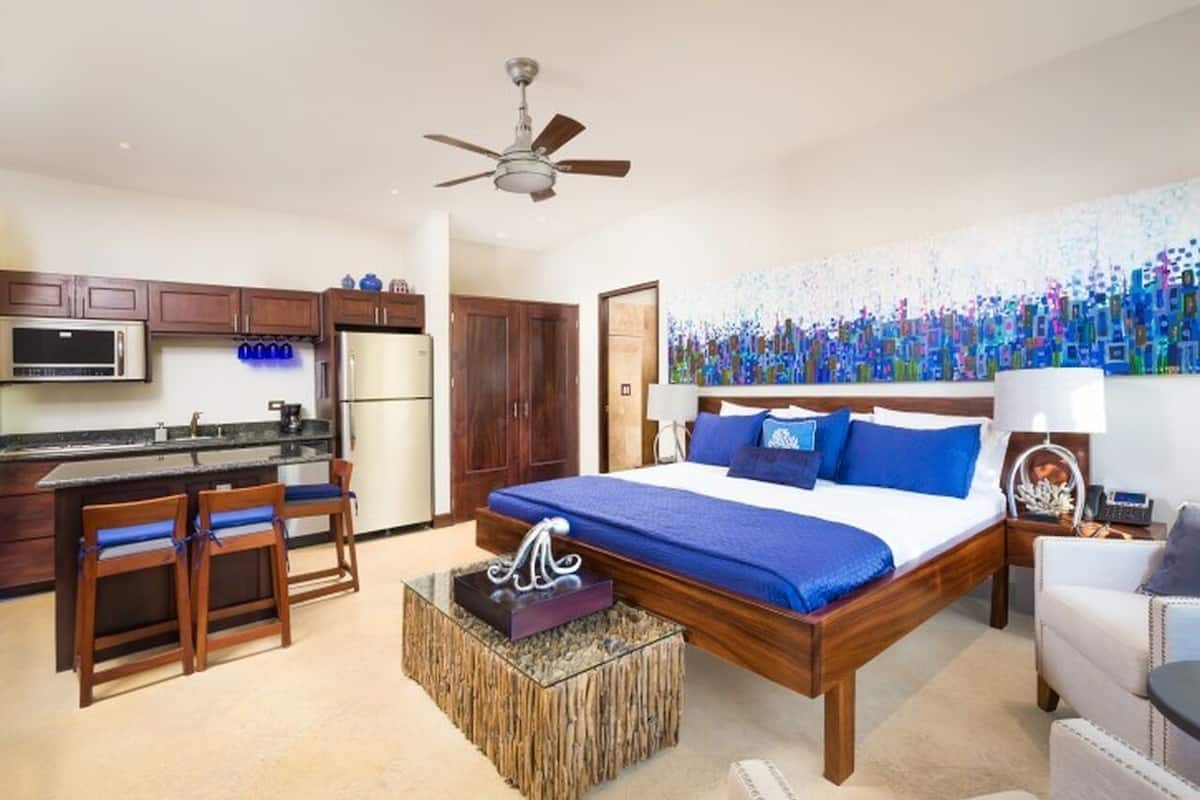 Una habitación de hotel con una cama de madera, kitchenette, zona de comedor y un ventanal grande.