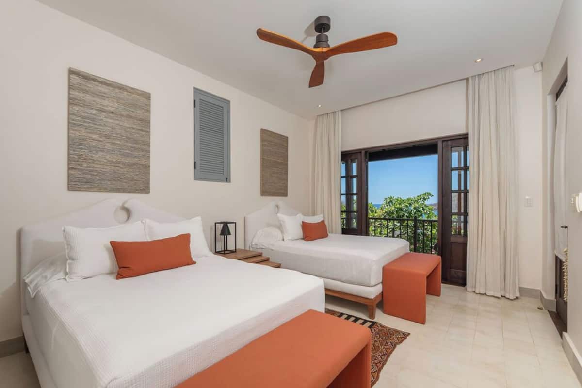 Habitación de hotel con dos camas, ventilador de techo, balcón con vistas y chimenea.