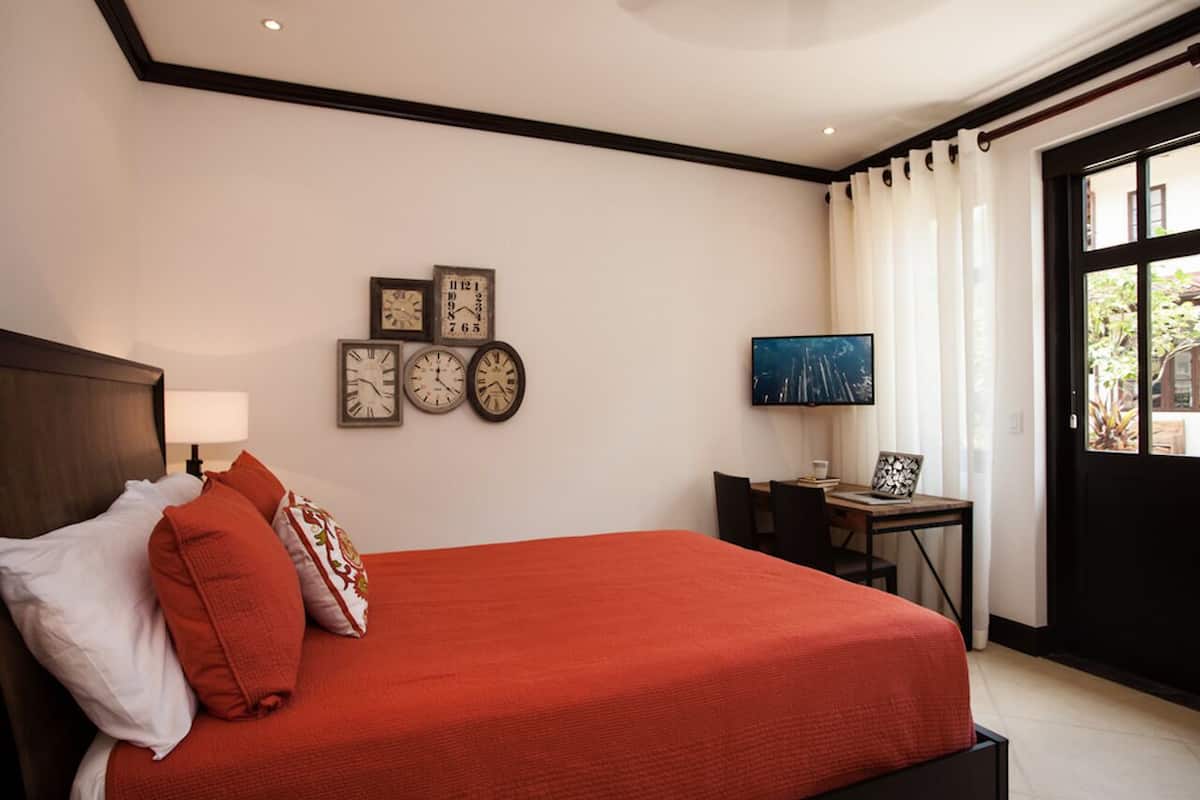 Una habitación de hotel con una cama grande, un escritorio con silla, televisión y ventana con cortinas.