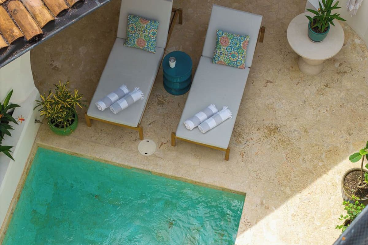 Vista aérea de un área junto a la piscina con dos sillones de descanso, una mesita redonda y plantas en macetas.