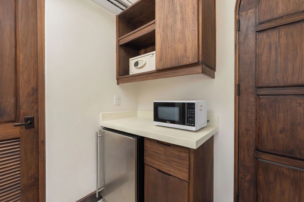 A compact kitchen with a microwave on a white countertop, wooden cabinets, and a stainless steel refrigerator.