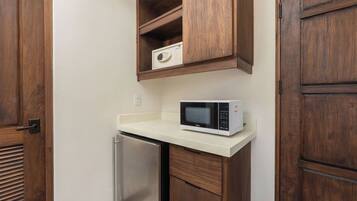 A compact kitchen with a microwave on a white countertop, wooden cabinets, and a stainless steel refrigerator.
