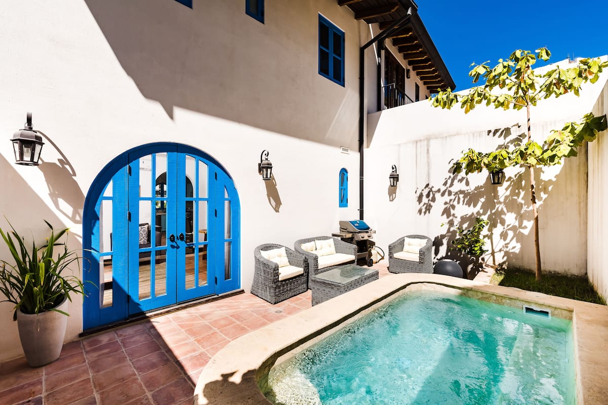 Zona de piscina con una puerta azul, mobiliario exterior y una planta en maceta.