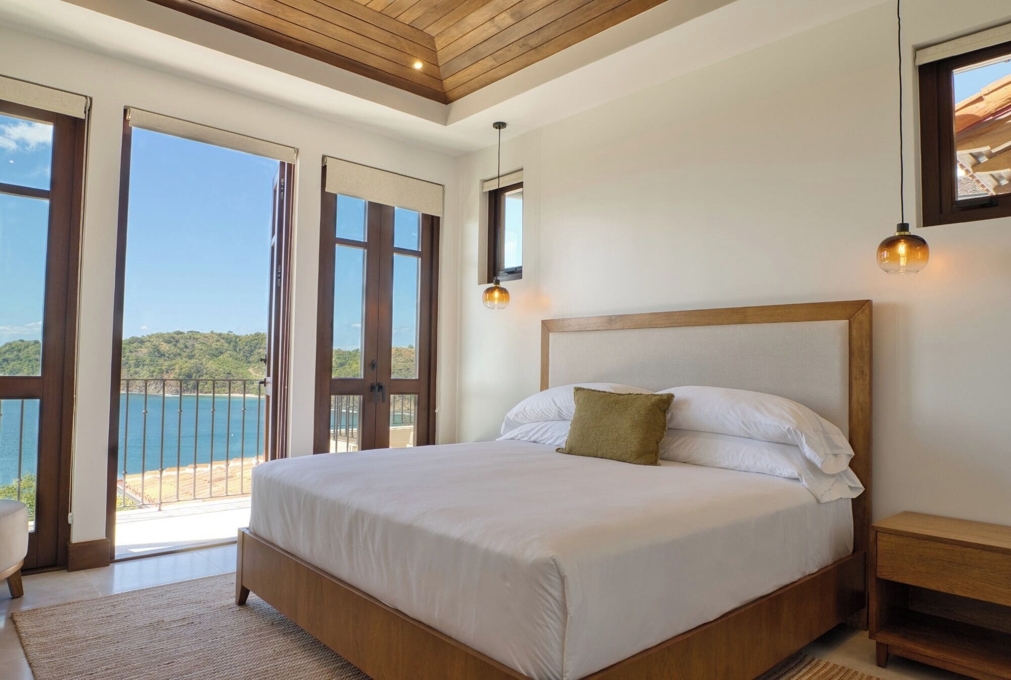 Ein Schlafzimmer mit einem großen Bett, einem Holz-Kopfteil und Blick auf das Meer durch offene französische Türen.