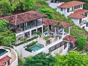 Un edificio residencial de varios pisos con piscina, mobiliario exterior y abundante vegetación.
