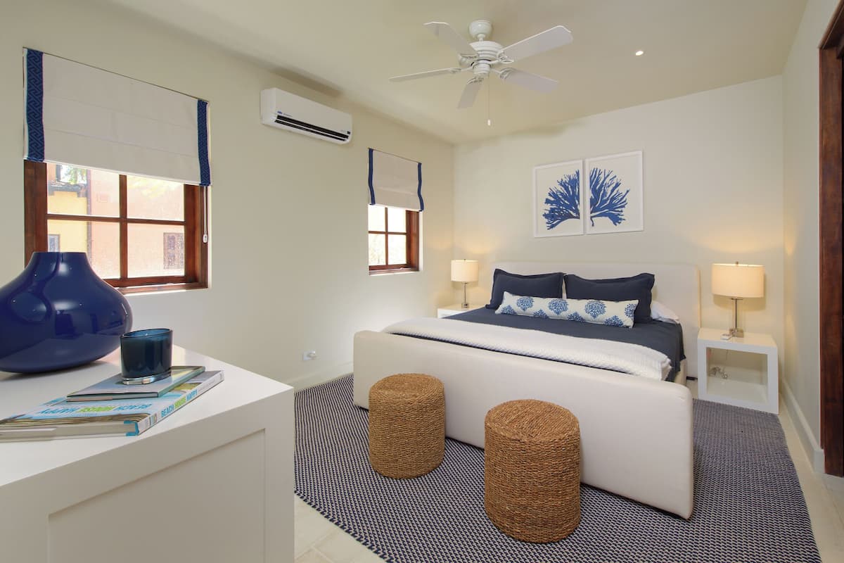 Un dormitorio moderno con cama, mesitas de noche, ventilador de techo y ventana con persianas.