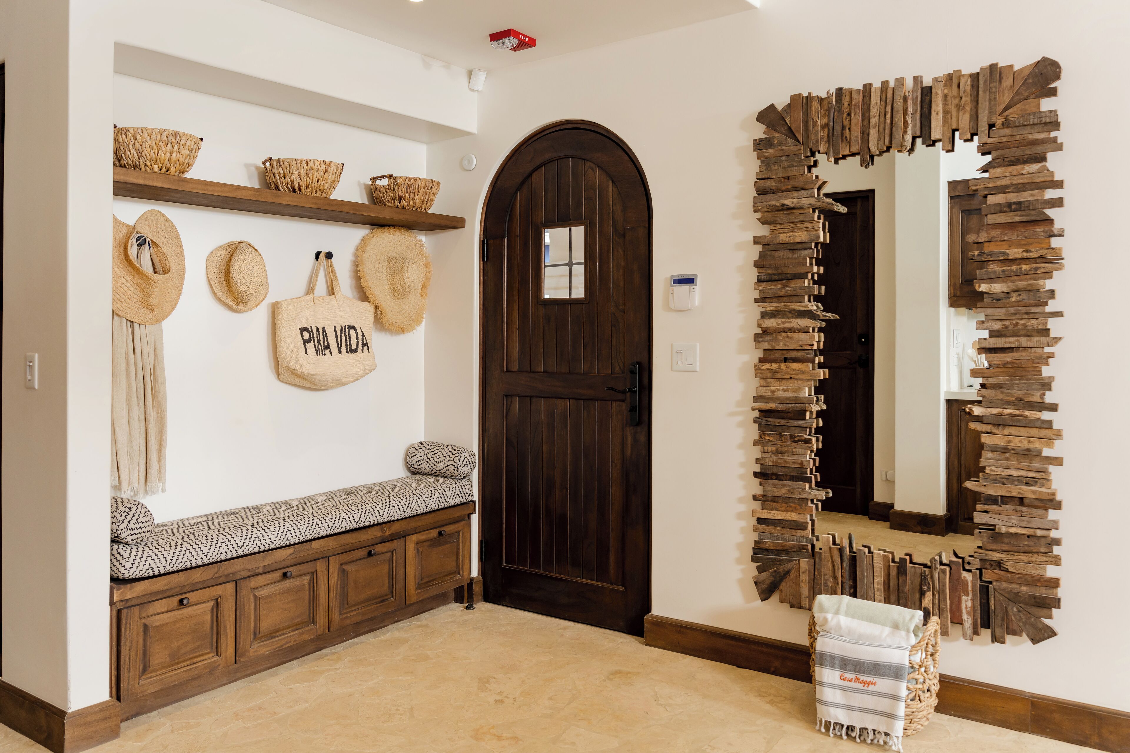 Un couloir avec un banc en bois, une porte en bois sombre et un miroir doté d’un cadre rustique.