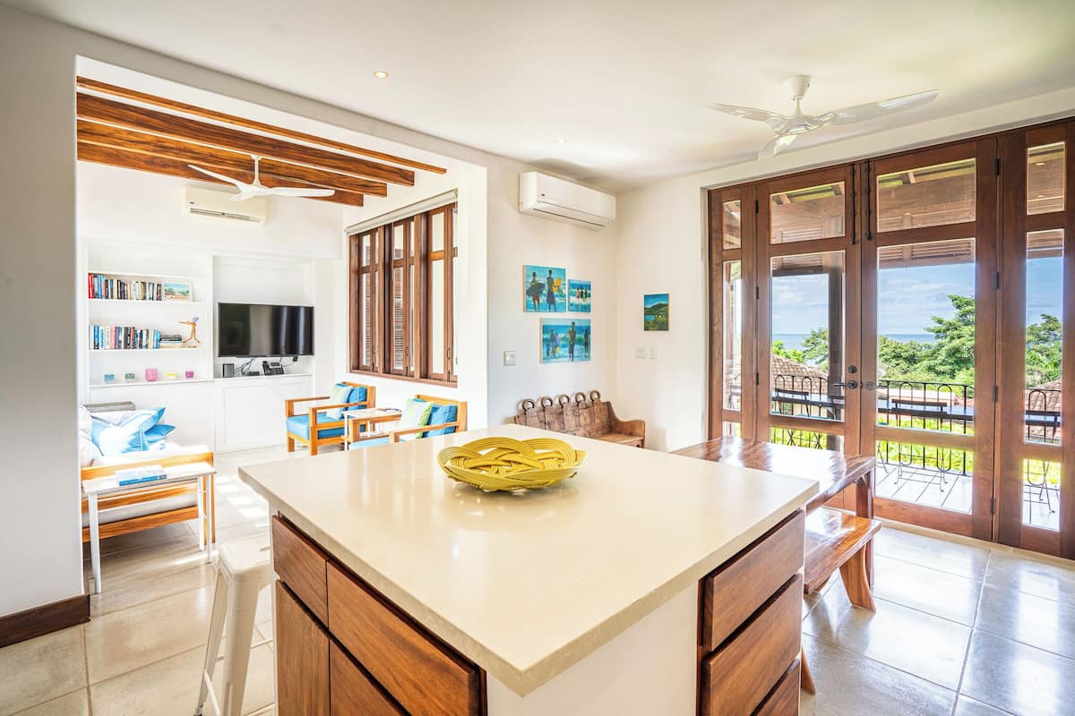 Una cocina amplia con una isla grande, armarios de madera y vistas al exterior a través de puertas correderas abiertas.