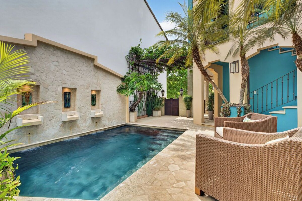 A swimming pool with a stone wall, wicker furniture, and a blue door.