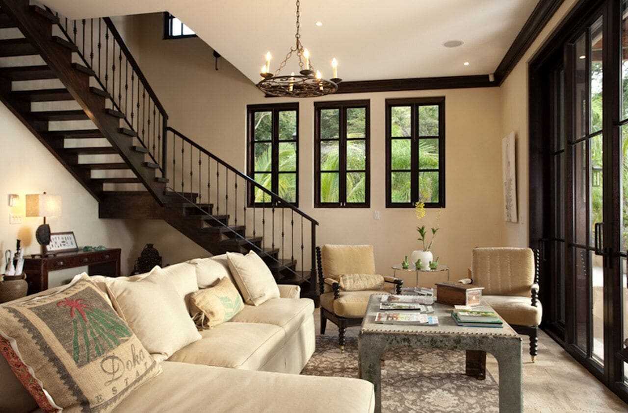 A spacious living room with a staircase, large windows, and a chandelier.