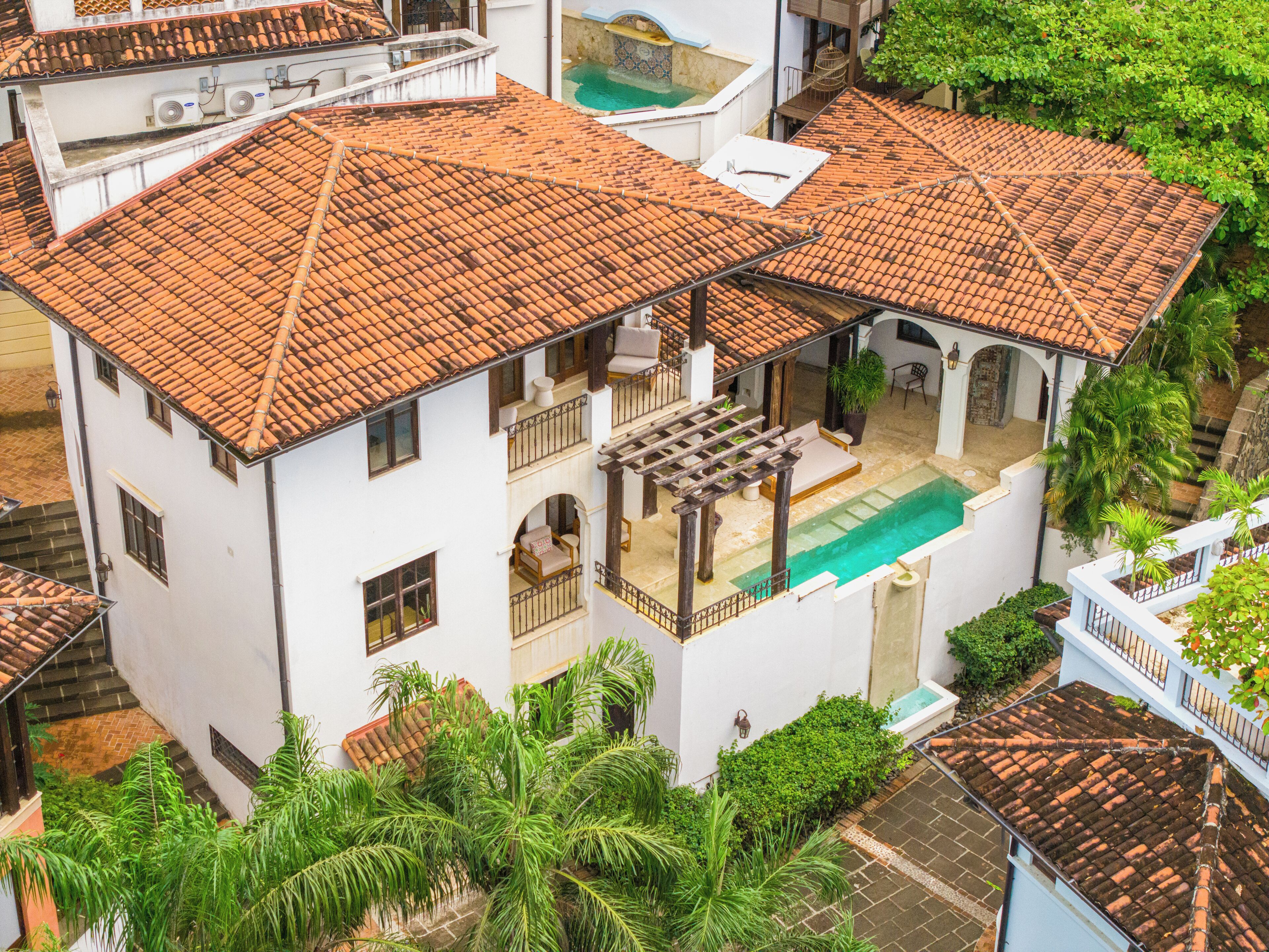A two-story building with a tiled roof, a swimming pool, and surrounding greenery.