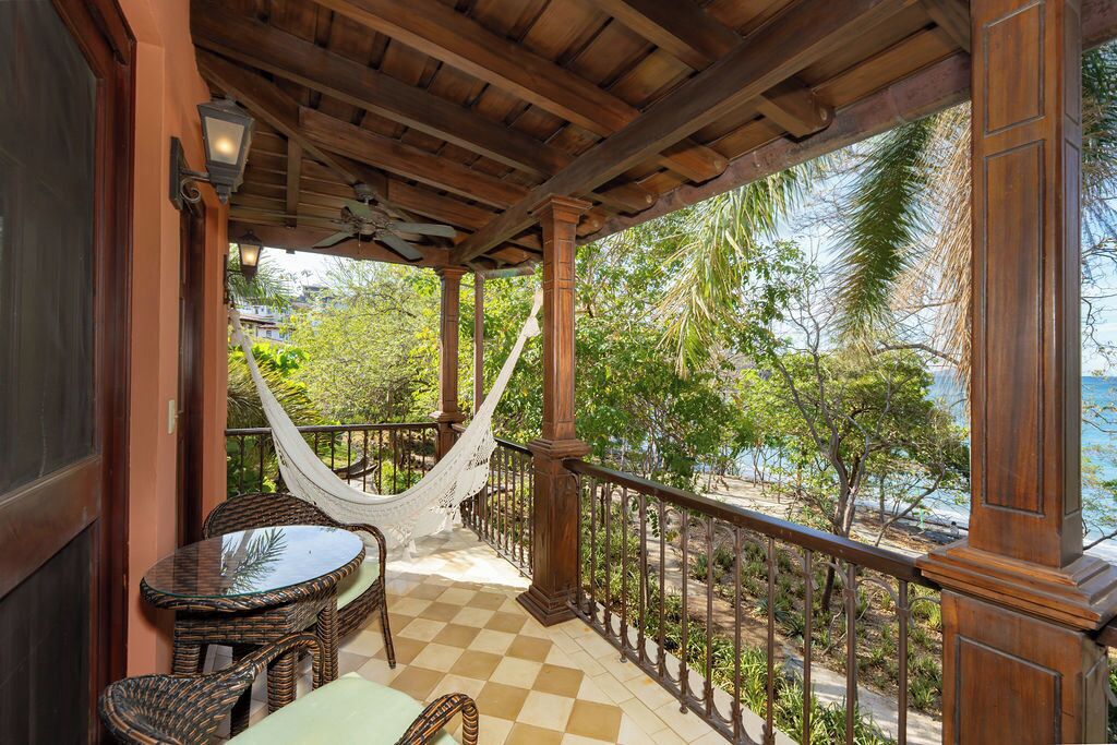 A covered balcony with a checkered floor, wicker furniture, and a hammock.