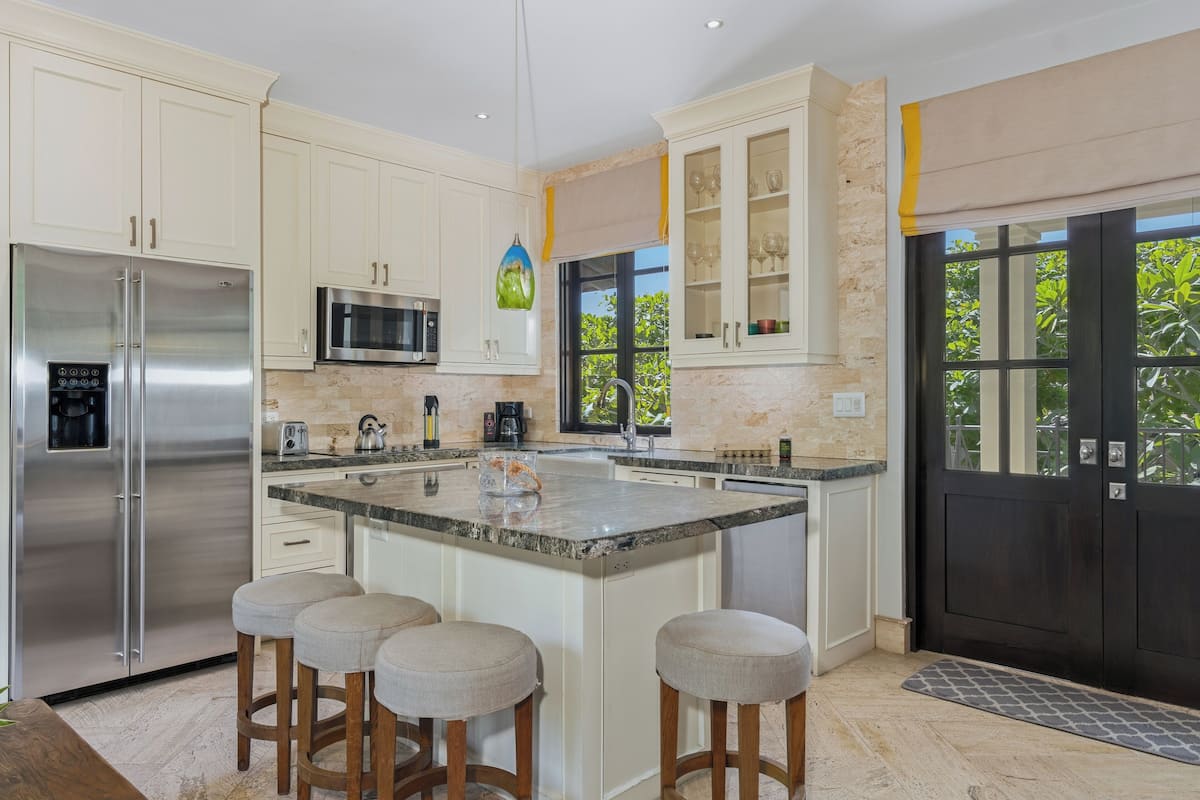 Una cocina moderna con gabinetes blancos, electrodomésticos de acero inoxidable y una isla grande con taburetes.