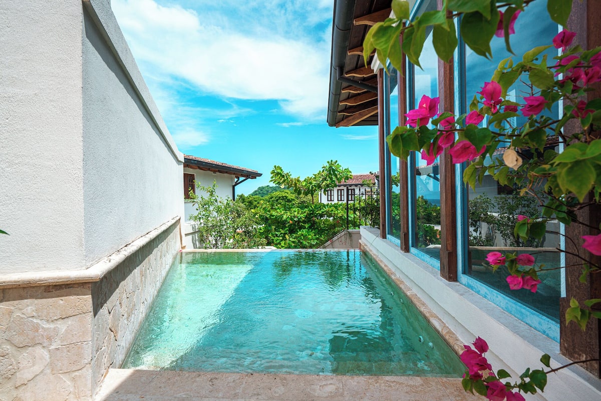Una piscina con agua cristalina azul, rodeada de muros de piedra y amplias ventanas.