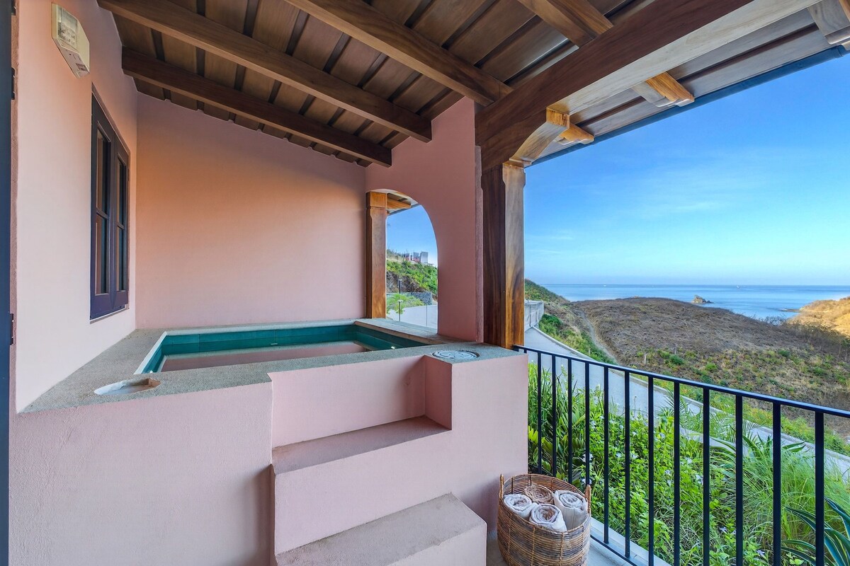 A balcony with a view of the coastline, a small pool, and steps leading to the balcony.