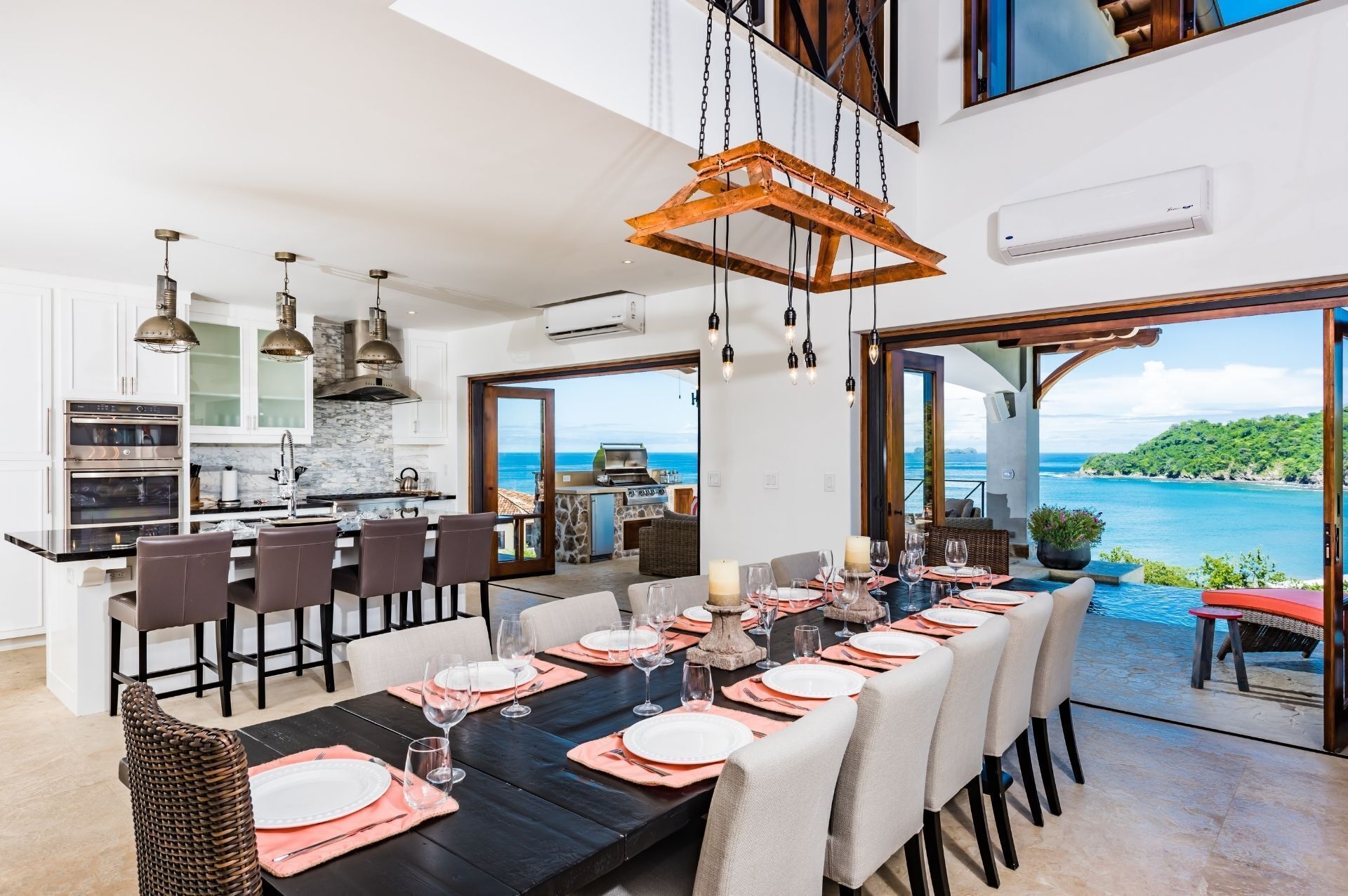 Una cocina moderna con electrodomésticos de acero inoxidable, un comedor con vistas al océano y una amplia estructura de techo de madera.