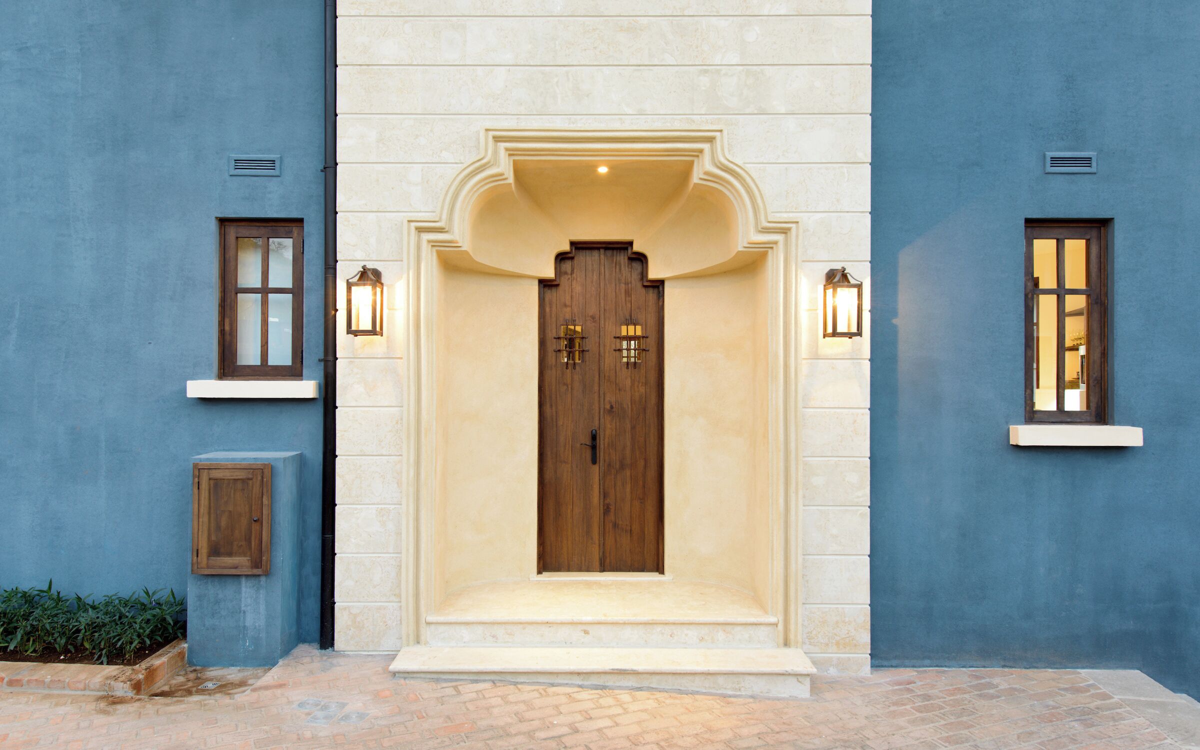 Un edificio con una puerta grande de madera, dos ventanas pequeñas con luces y un armario pequeño.